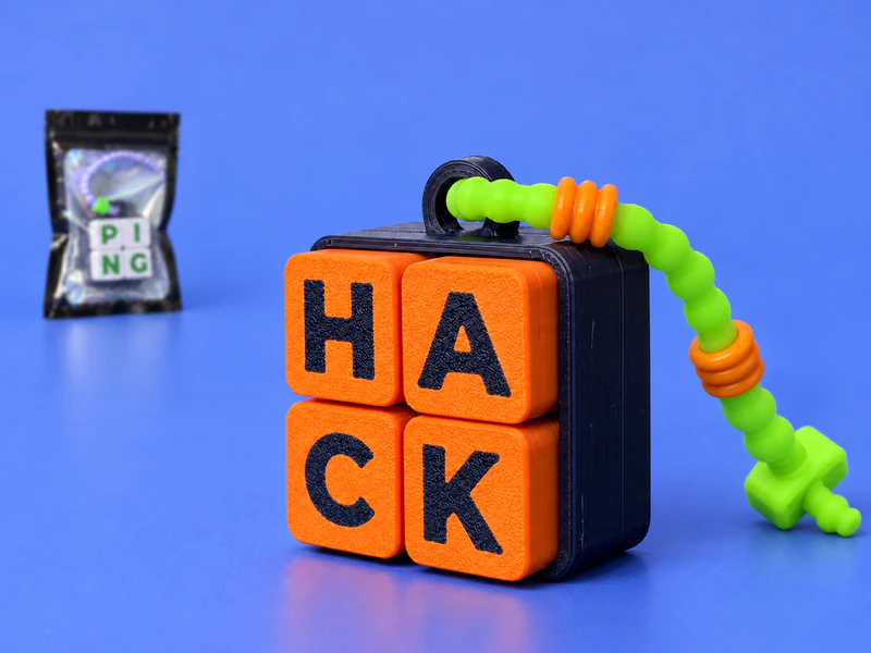 Il clicker HACK in primo piano su carta blu: quattro tasti arancio con le lettere blu notte e il cordino lime